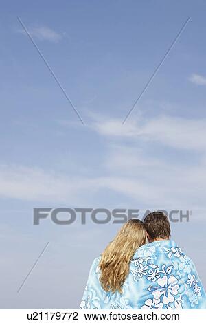 Stock Image - Teenage couple hugging under towel on beach. Fotosearch