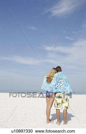 Stock Image - Teenage couple sharing towel on beach. Fotosearch