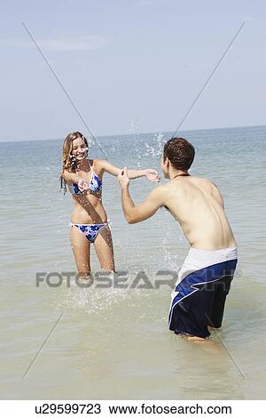 Stock Image - Teenage couple splashing each other in ocean. Fotosearch