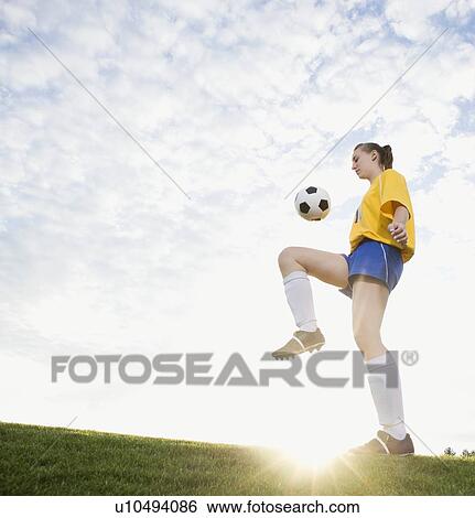 Stock Photograph - Teenage girl bouncing soccer ball on knee. Fotosearch