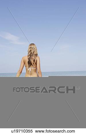 Stock Photography - Teenage girl holding inflatable ring contemplating ocean waves. Fotosearch