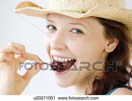 Stock Image - Teenage girl in cowboy hat eating cherry. Fotosearch