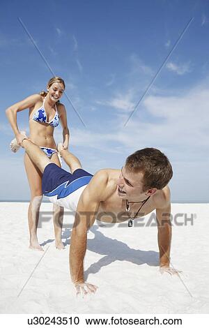 Stock Image - Teenage girl pushing boyfriend on beach. Fotosearch