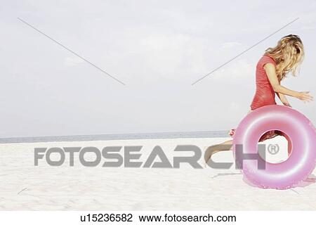 Teenage girl rolling inflatable ring on beach View Large Photo Image Stock Image - Teenage girl rolling inflatable ring on beach. Fotosearch