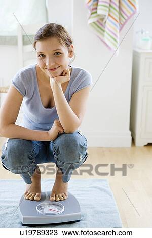 Stock Image - Teenage girl standing on bathroom scale. Fotosearch