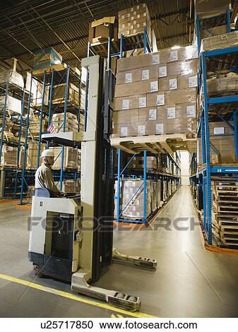 Stock Image - Warehouse worker driving forklift. Fotosearch
