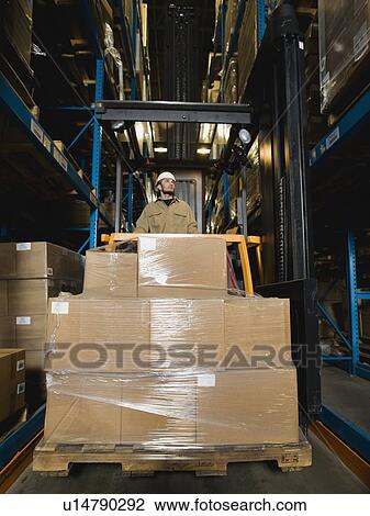 Stock Image - Warehouse worker driving forklift with palette. Fotosearch