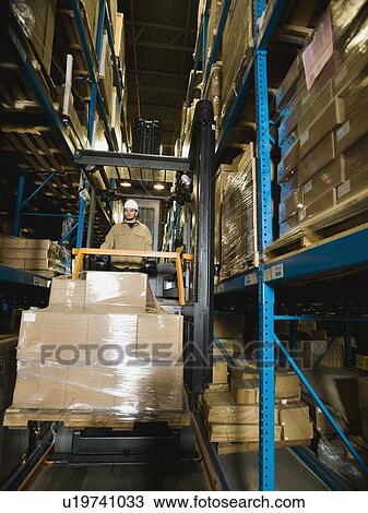 Stock Image - Warehouse worker driving forklift with palette. Fotosearch