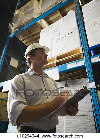 Picture - Warehouse worker writing on clipboard. Fotosearch