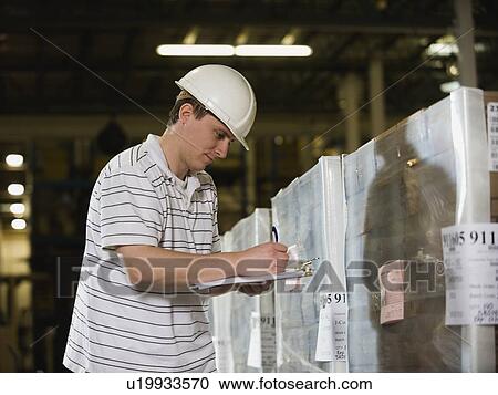 Stock Image - Warehouse worker writing on clipboard. Fotosearch