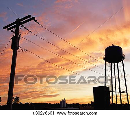 Stock Image - Water tower and telephone pole against sunset sky. Fotosearch