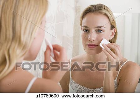 Stock Image - Woman applying makeup in bathroom. Fotosearch