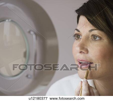 Stock Photo - Woman applying makeup in vanity mirror. Fotosearch