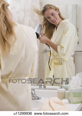 Stock Photograph - Woman blow-drying hair in bathroom. Fotosearch