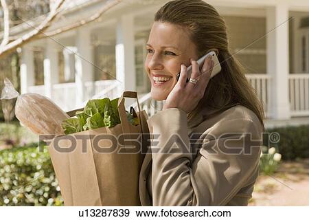 Woman carrying groceries and talking on telephone View Large Photo Image Stock Photo - Woman carrying groceries and talking on telephone. Fotosearch