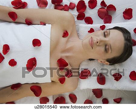 Stock Image - Woman covered in flower petals laying on massage table. Fotosearch