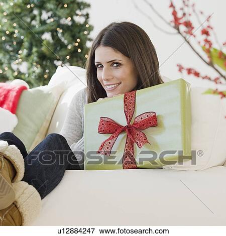 Woman holding gift on sofa View Large Photo Image Stock Photo - Woman holding gift on sofa. Fotosearch