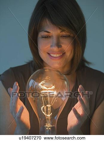Stock Image - Woman holding hands around large light bulb. Fotosearch