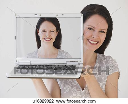 Stock Image - Woman holding laptop next to face. Fotosearch