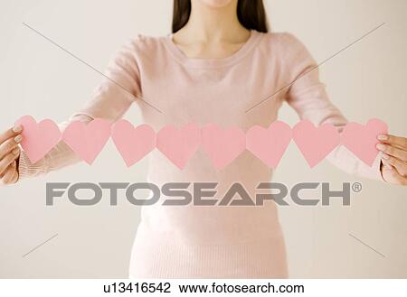 Stock Image - Woman holding string of cut out hearts. Fotosearch