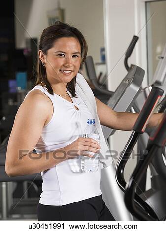 Stock Image - Woman holding water bottle on exercise machine. Fotosearch
