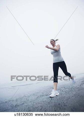 Stock Photography - Woman jogging on foggy beach. Fotosearch