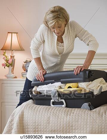 Stock Photograph - Woman packing full suitcase. Fotosearch