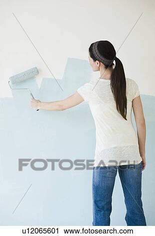 Stock Image - Woman painting wall with paint roller. Fotosearch