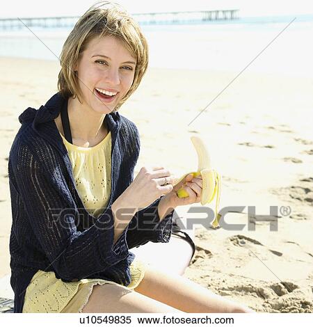Stock Photography - Woman peeling banana at beach. Fotosearch