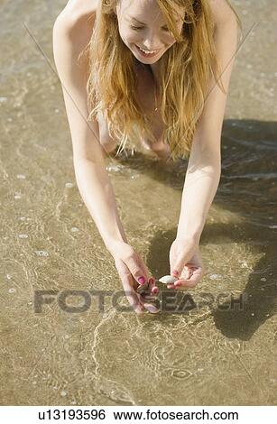 Stock Photograph - Woman picking up seashells at beach. Fotosearch