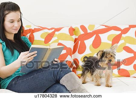Stock Photo - Woman reading on sofa next to dog. Fotosearch