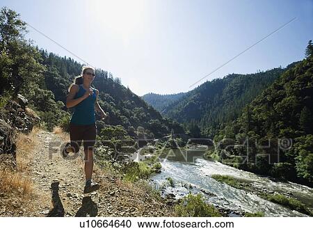 Stock Image - Woman running on riverside trail. Fotosearch