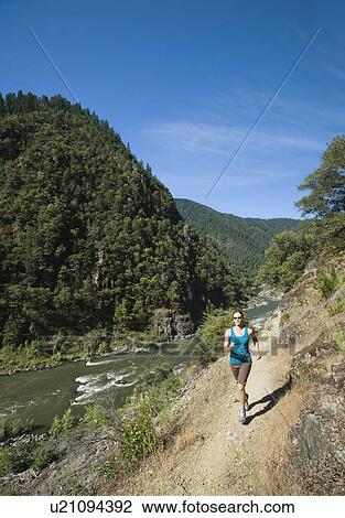 Stock Image - Woman running on riverside trail. Fotosearch