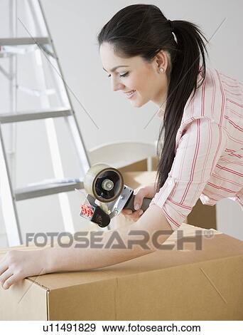 Stock Photo - Woman sealing moving box with tape. Fotosearch