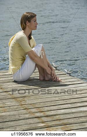Stock Photograph - Woman sitting on dock. Fotosearch