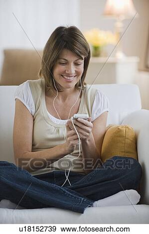 Stock Photo - Woman sitting on sofa and listening to mp3 player. Fotosearch