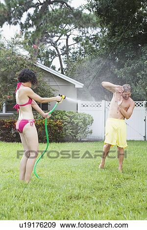 Stock Photo - Woman spraying man with hose in backyard. Fotosearch