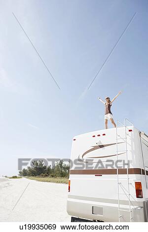 Stock Photo - Woman standing on motor home with arms outstretched. Fotosearch