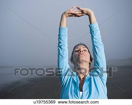 Stock Photo - Woman stretching on foggy beach. Fotosearch