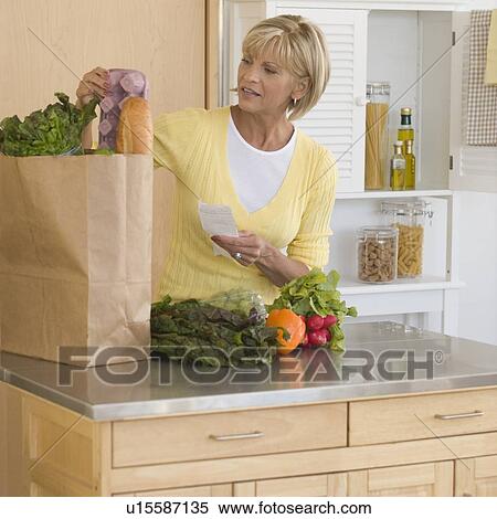 Stock Photography - Woman unpacking groceries in kitchen. Fotosearch