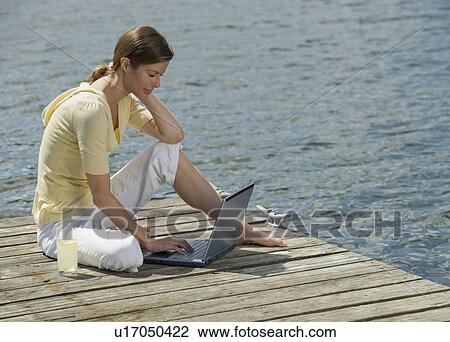 Stock Image - Woman using laptop on dock. Fotosearch