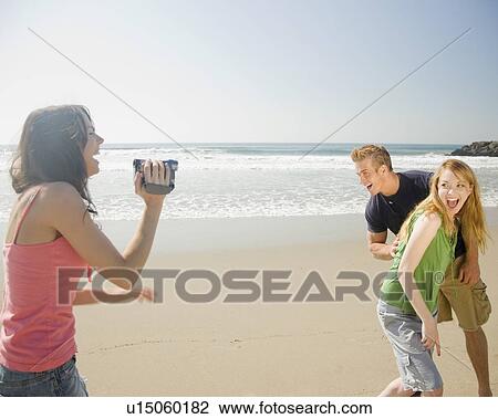 Stock Image - Woman video recording friends at beach. Fotosearch