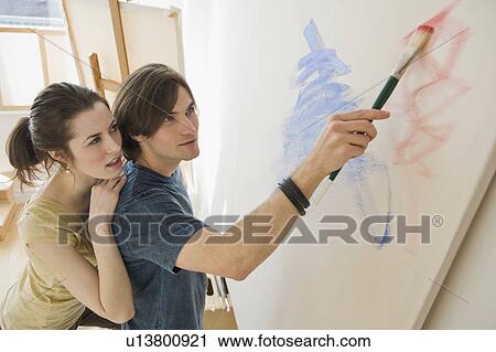 Stock Image - Woman watching boyfriend paint on easel. Fotosearch
