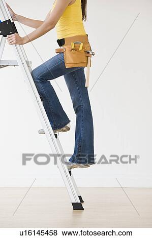 Stock Photo - Woman wearing tool belt climbing ladder. Fotosearch