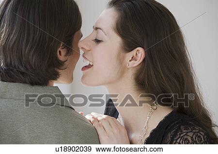 Stock Photo - Woman whispering in boyfriend’s ear. Fotosearch