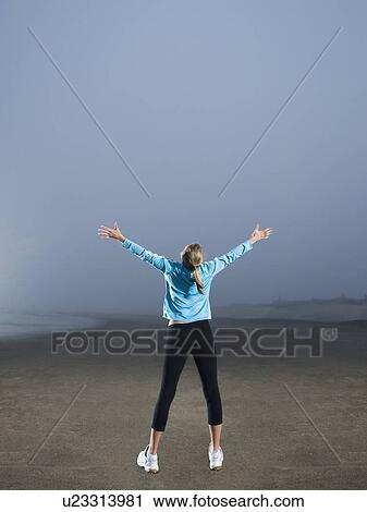 Stock Image - Woman with arms outstretched on foggy beach. Fotosearch