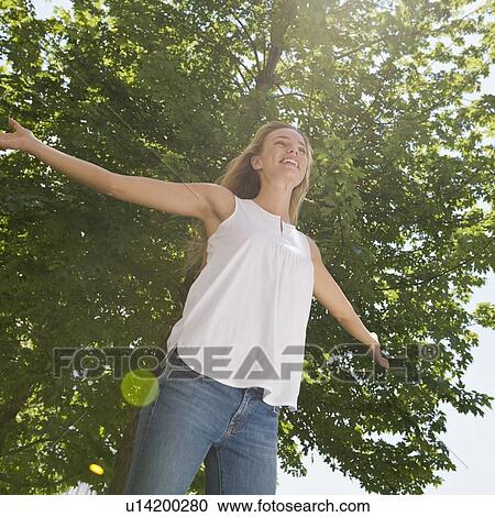 Woman with arms outstretched standing under tree View Large Photo Image Stock Image - Woman with arms outstretched standing under tree. Fotosearch