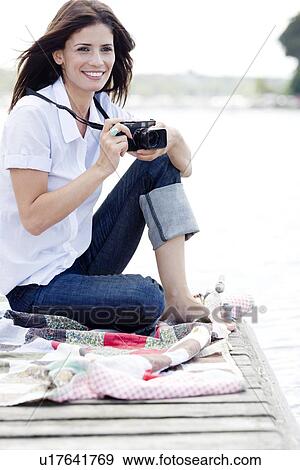 Stock Photo - Woman with camera sitting on dock. Fotosearch