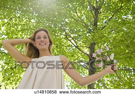 Stock Photo - Woman with flowers standing under tree. Fotosearch
