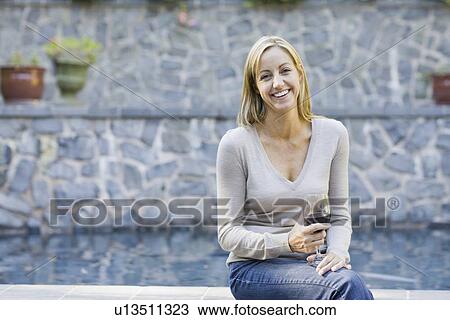 Stock Image - Woman with wine glass sitting on edge of swimming pool. Fotosearch